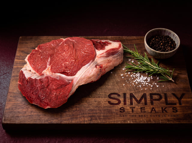 Raw ribeye steak on a Simply Steaks wooden board with rosemary and black pepper