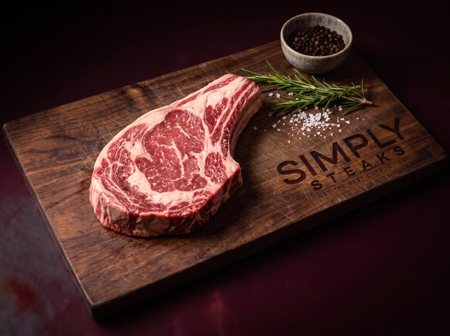 Bone-in ribeye steak on a Simply Steaks wooden board with rosemary